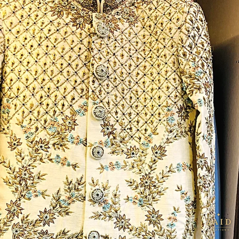 Close-up of gold trellis embroidery with pastel florals on a cream sherwani